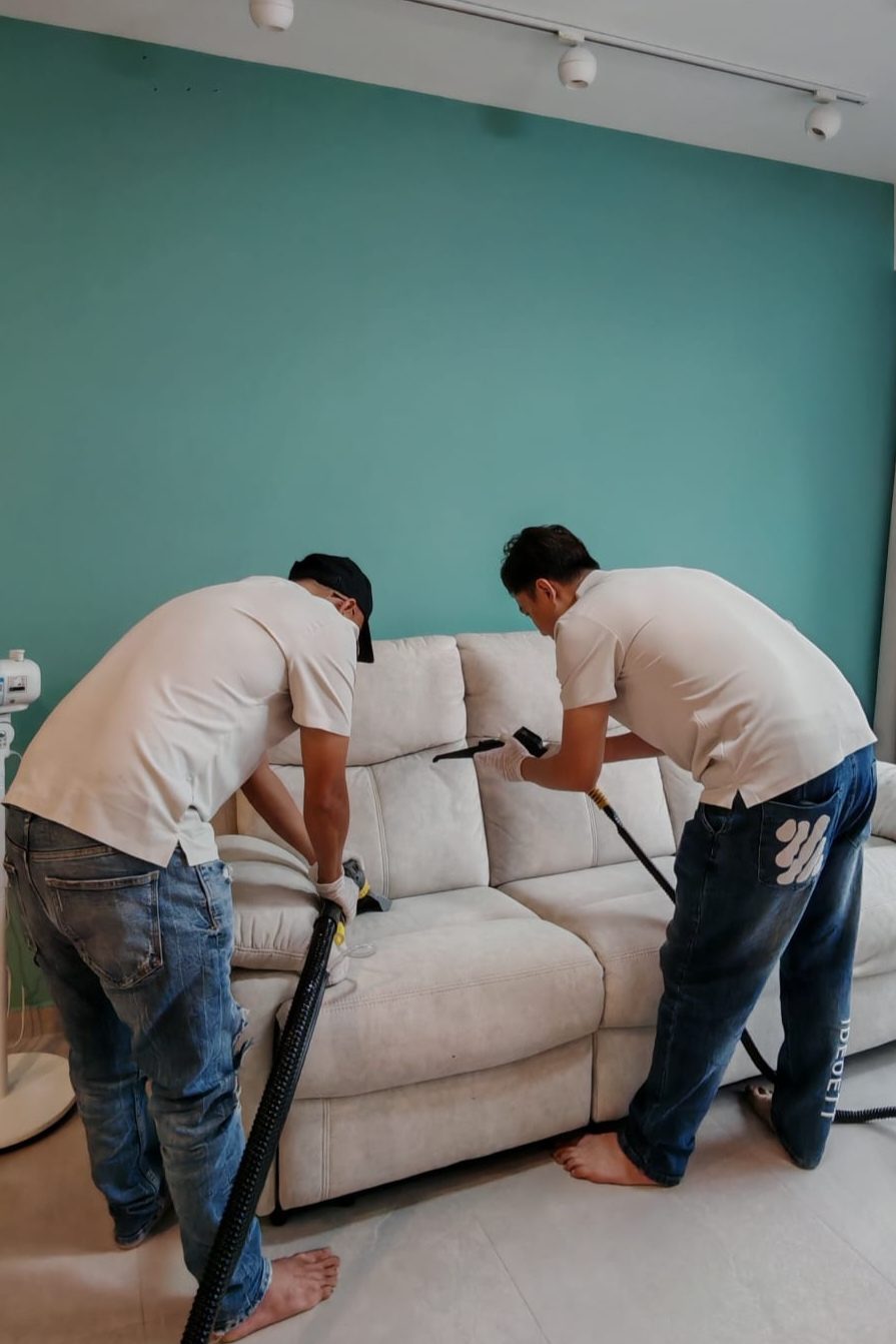 Two UltraRevive technicians deep-cleaning a fabric sofa in a Singapore living room